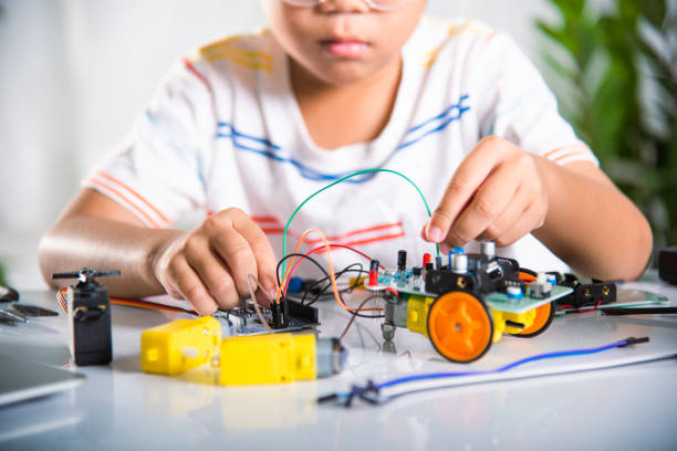 Asian kid boy plugging energy and signal cable to sensor chip with open-source hardware and software robot car, Little child remotely learn online with car toy, STEAM education AI technology course school learning lesson