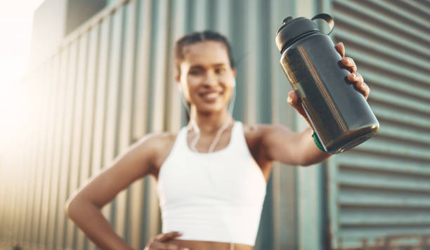 Closeup of one fit young hispanic woman holding a water bottle with the word "run" displayed in a digital time font while exercising in an urban setting outdoors. Female athlete taking a break to quench thirst and cool down after cardio training workout Closeup of one fit young hispanic woman holding a water bottle with the word "run" displayed in a digital time font while exercising in an urban setting outdoors. Female athlete taking a break to quench thirst and cool down after cardio training workout quench your thirst pictures stock pictures, royalty-free photos & images