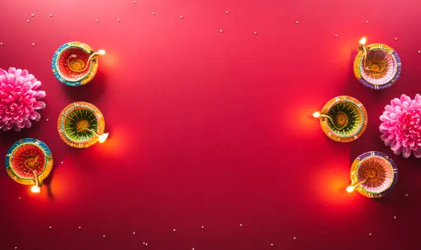 Photo of Happy Diwali - Clay Diya lamps lit during Diwali, Hindu festival of lights celebration. Colorful traditional oil lamp diya on red background