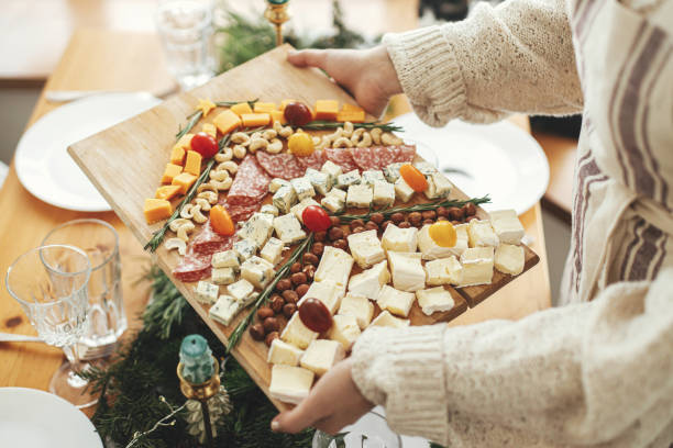 Cheese appetizers and salami in shape of christmas tree, creative food arrangement for christmas holidays. Woman holding cheese board on background of festive table with fir branches. Antipasto stock photo