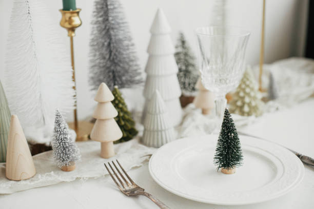 istock Stylish Christmas table setting. Modern little christmas tree on plate, vintage cutlery, wineglass, modern christmas trees and houses on white rustic table. Holiday brunch, new year celebration 1424142230