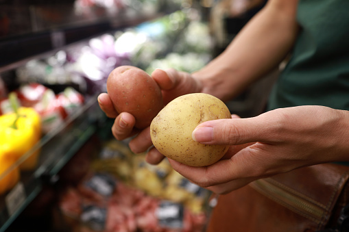 Young Asian woman doing grocery shopping in a supermarket, close up of her hand choosing potatoes. Healthy eating lifestyle.