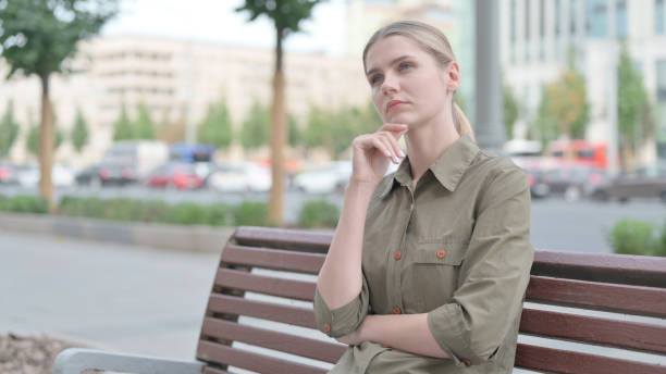 istock Pensive Woman Thinking while Sitting Outdoor on Bench 1424160164