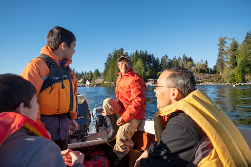 Mature Asian man operating a small boat with a father and 2 teenaged sons heading out to open water to fish for salmon.  Bamfield, Vancouver Island, British Columbia, Canada