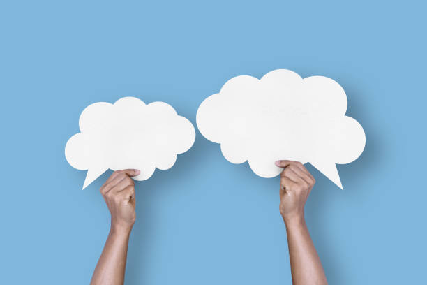 istock hand holding white paper cloud shape speech bubble balloon isolated on light blue background. 1424162002