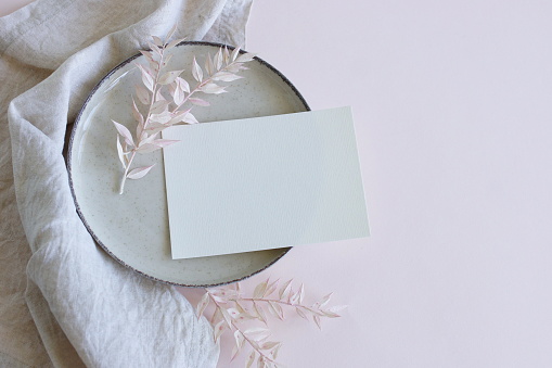 Blank paper sheet card mockup on plate with copy space, linen napkin and dry flowers top view neutral colors .Wedding invitation, menu. Scandinavian style.