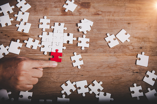 Hands holding jigsaw puzzles piece on wooden table background, success business, solution strategy, teamwork partnership concept
