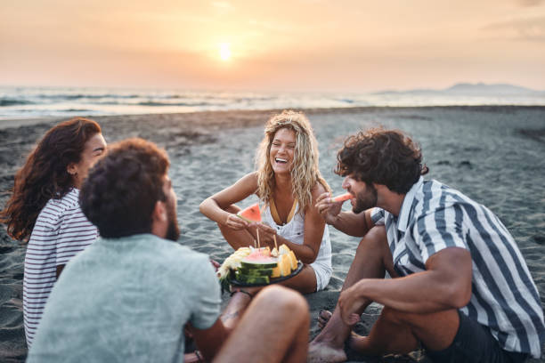 istock Happy couples talking while eating fruit on the beach at sunset. 1424166606