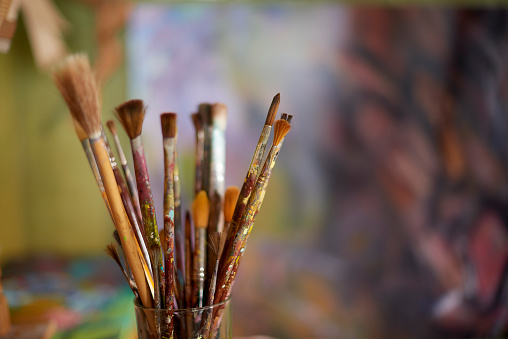 Many paint brush in a workshop, studio or room with blurred background. Dirty, untidy and used wooden brush tools or equipment in a glass cup in an artistic, creative and craft painting workspace