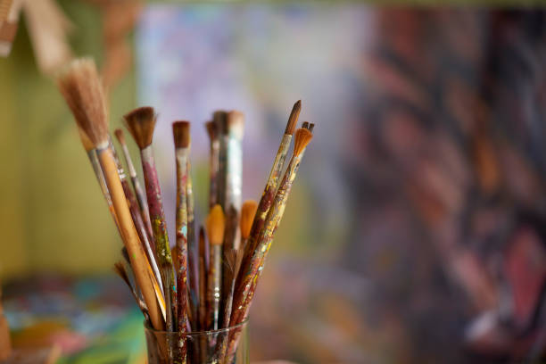 Many paint brush in a workshop, studio or room with blurred background. Dirty, untidy and used wooden brush tools or equipment in a glass cup in an artistic, creative and craft painting workspace stock photo