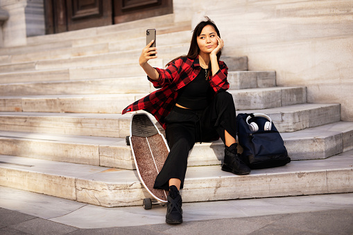 Young smiling woman taking selfie photo. Urban girl with skateboard