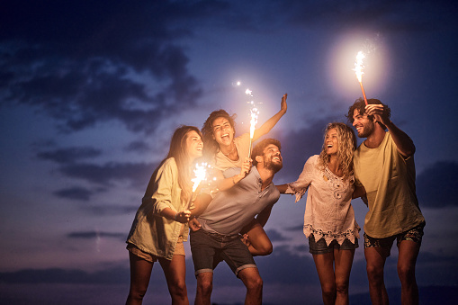 Group of cheerful friends having fun with burning torches during the night on the beach. Copy space.
