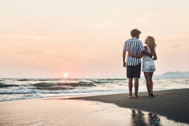 istock Back view of embraced couple talking on the beach at sunset. 1424168687