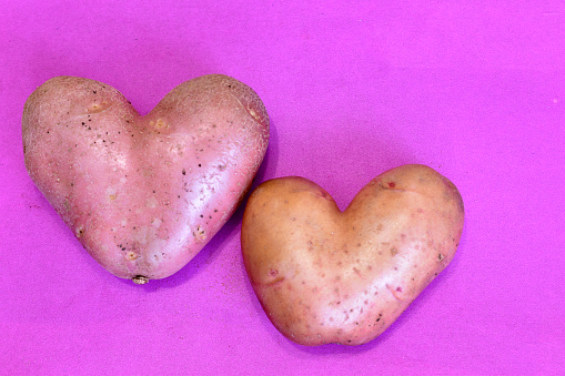 In the picture, on a pink background, there are potato fruits that look like a heart.
