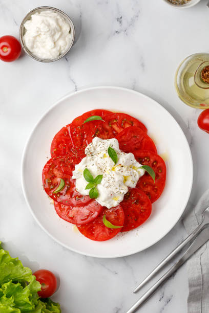 istock Stracciatella cheese salad on marble background with fork, oil, basil and tomatoes. Top view 1424173972