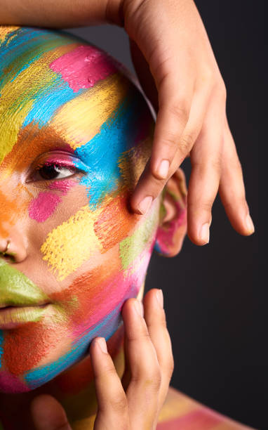 istock Model with face color paint use hand to gesture for art against black wall or studio background. Woman with abstract makeup on skin and nose piercing, show eye in creative design or dark portrait. 1424180443
