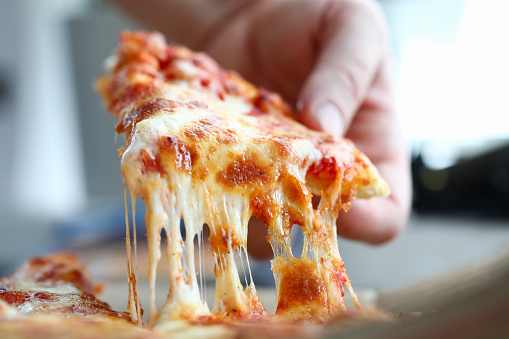 Male arm taking slice of cheesy tasty fresh pizza close-up