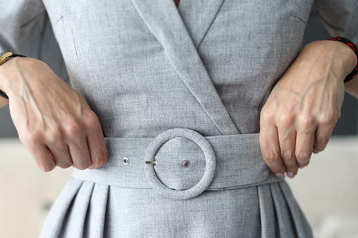 Woman straightening her belt on gray dress with her hands close-up. Trying on clothes for home delivery concept