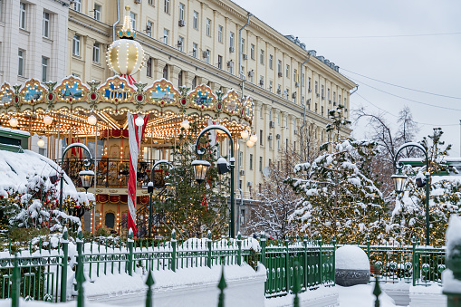 Festive Merry-go-round carousel in winter Square in Moscow among christmas treees. Magic snowy cityscape.