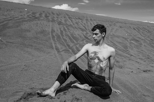 Man sitting on the sand in sandy desert. Black and white