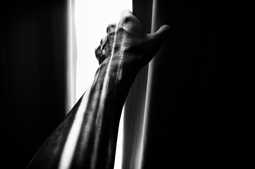 An image of a hand opening the curtain and the sunlight