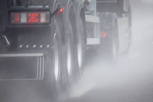 Close-up of truck bottom driving on wet road in rain or fog. Water splashes spray from under vehicle wheels. Low visibility on highway. Selective focus Close-up of truck bottom driving on wet road in rain or fog. Water splashes spray from under vehicle wheels. Low visibility on highway. Selective focus. truck rain stock pictures, royalty-free photos & images