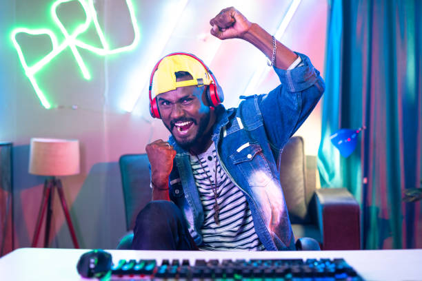istock Excited gamer with headset celebrating victory by shouting while playing live video game by looking camera at home - concept of achievement, competition and tournament. 1424185342