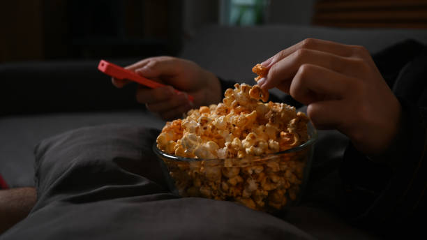 istock Close up view man hand grabbing popcorn and watching television at night. Leisure activity, relaxation, hobby concept. 1424186160