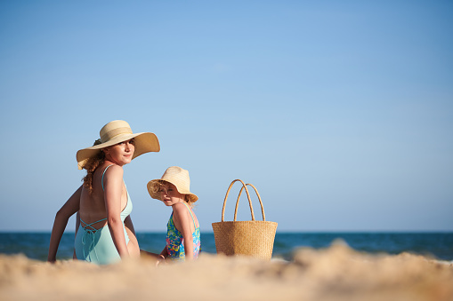 Mother and daughter in straw hats sunbathing on beach