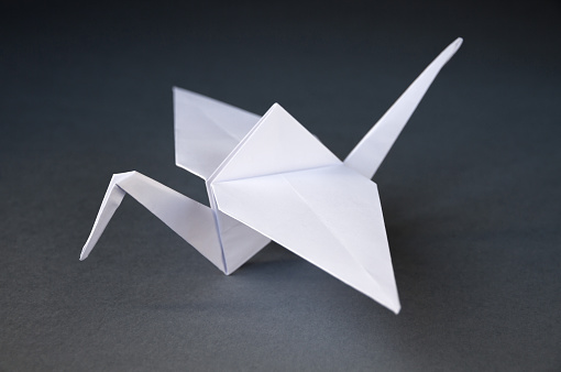 White paper crane origami isolated on a blank grey background.