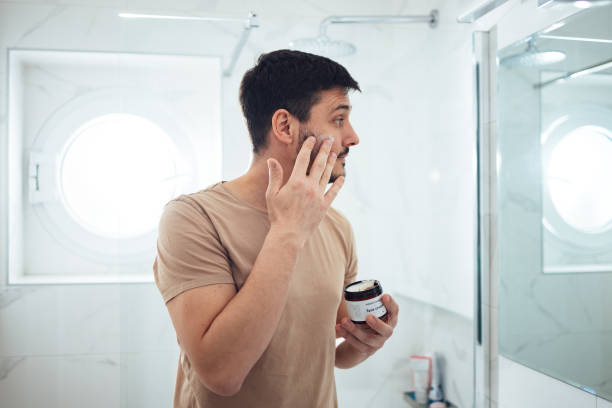 istock Handsome Man Applying Face Cream in the Bathroom (Copy Space) 1424187814