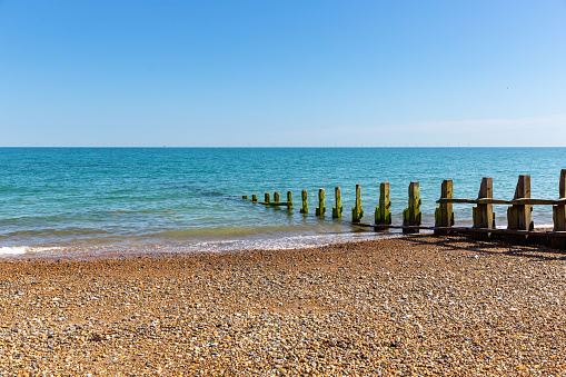 Lancing, West Sussex, UK, 2021: A groyne on a pebble beach disappears into a very blue sea. Wind farm barely visible in background.