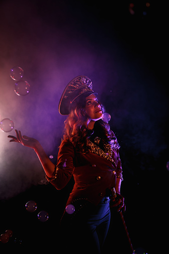 Female magician illusionist circus with stylish hat in shows soap bubbles show at black background. Woman actress theatrical clothes in stage costume. Concept of theatre performance. Copy space