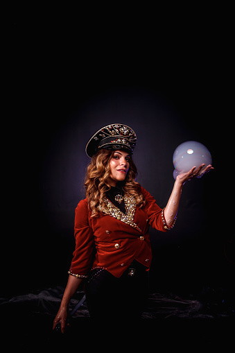 Woman magician illusionist circus with stylish hat in shows soap bubbles show at black background. Female actress theatrical clothes in stage costume. Concept of theatre performance. Copy space