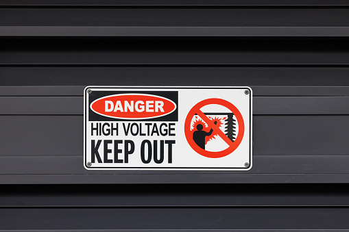 Danger, high voltage, keep out sign on a gray wall.