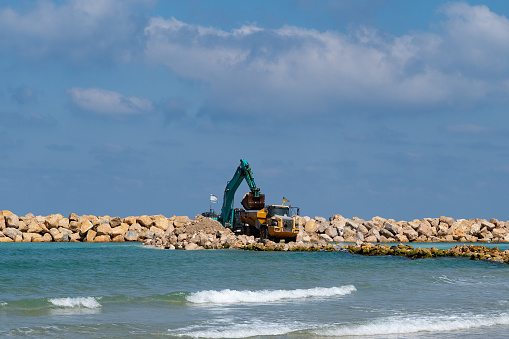 An excavator and a mining truck move stones into the sea. Construction of breakwaters to protect the beach in Netanya in Israel.