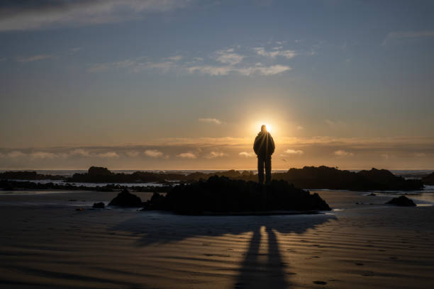 Man watching sunrise at a rocky beach.  Catlins, South Island.