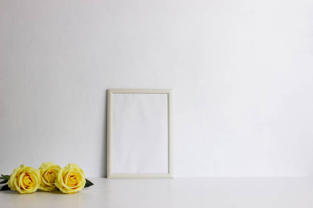 istock ellow roses with white photo frame over the white wall with natural light. 1424198548