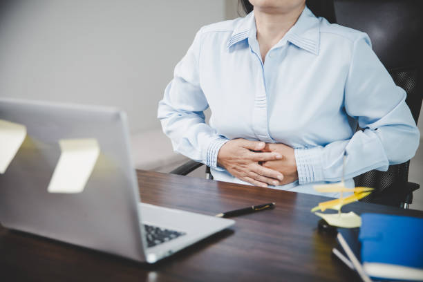 Young asian business woman person sitting at work and has stress pain in her stomach. Concept office syndrome abdomen pain from occupational disease, Female having belly pain and using laptop computer stock photo