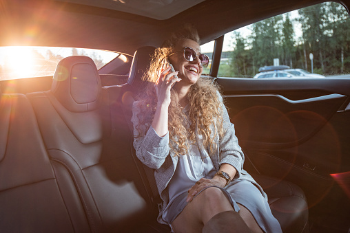 Young businesswoman sitting in car and using cell phone