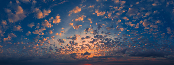 Colorful sunset with many small orange clouds in a sky. Panoramic format.
