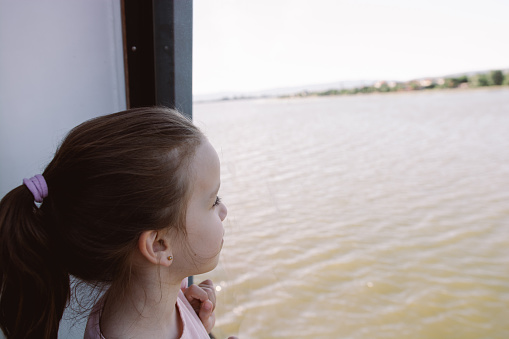 Girl looking trough window on a river while traveling by boat