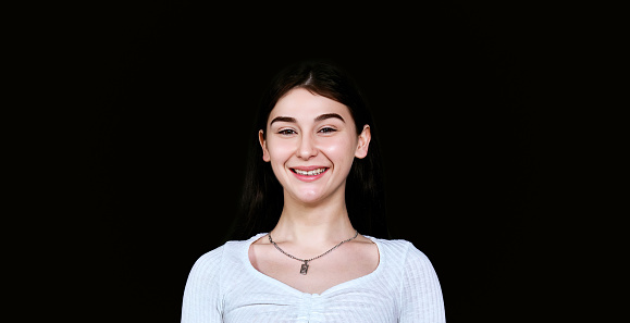 Portrait of beautiful young asian woman with smile on her face
in white blouse with long dark hair on dark background, looking at camera. studio shot.