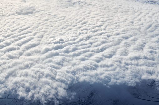 Over clouds top view from aircraft window, thick white blue clouds looks like soft foam, overcast with fresh frosty air. Beautiful cloudy sky view to troposphere, heavy cloudiness