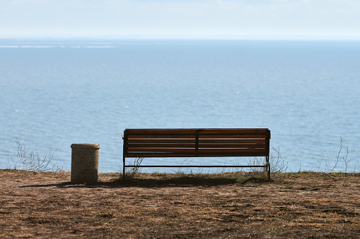 Empty bench with trashcan on cliff before sea background, peaceful and quiet place for thinking alone, loneliness and loss of loved one concept. Pacifying view of marine horizon of Azov sea copy space