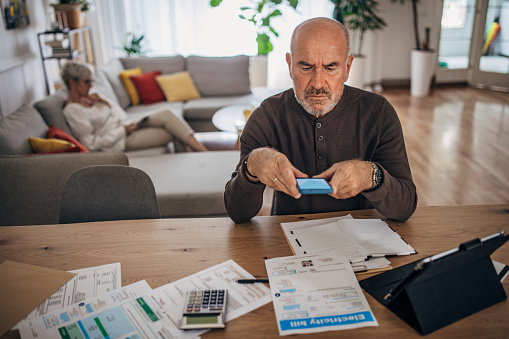 Mature man at home looking at the bills and taxes and trying to calculate and pay them