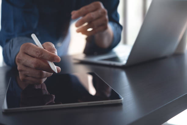 istock Close up of business man using digital tablet and working on laptop computer on office table 1424224395