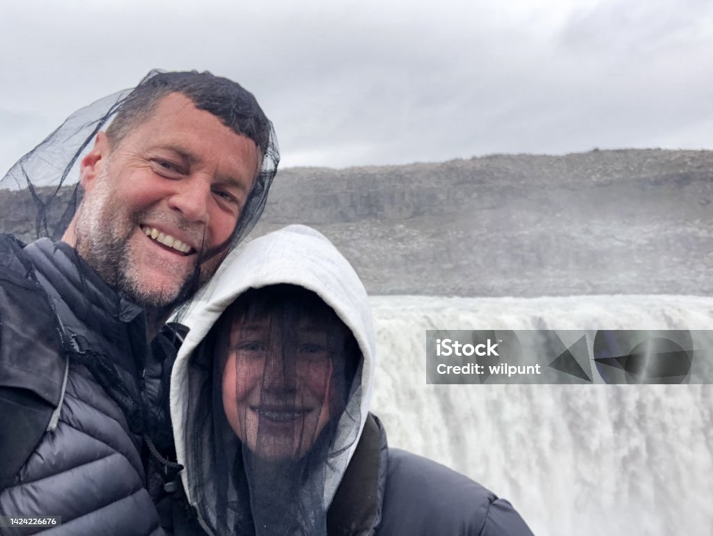 Father and Son happy selfie wearing head nets protection against midges chironomids at powerful waterfall Father and Son happy selfie wearing head nets protection against midges chironomids at Dettifoss Waterfall on the Diamond Circle, Jökulsá á Fjöllum River, Vatnajökull National Park, North East Iceland Midge Fly Stock Photo
