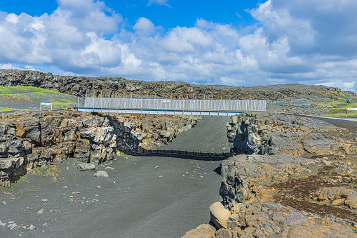 Landscape on Iceland of Reykjanes Peninsula. Metal bridge over the North American and Eurasian rifts. Lava stones with black sand and green grass in sunshine and clouds