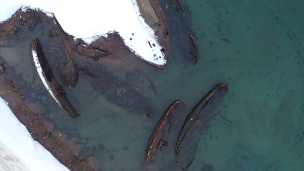 Top view of many old wrecked ships drowned at the sea shore in snowy winter season. Footage. Aerial view of the ruined boats in the cold water near snowy coast. Top view of many old wrecked ships drowned at the sea shore in snowy winter season. Aerial view of the ruined boats in the cold water near snowy coast. fishing boat sinking stock pictures, royalty-free photos & images